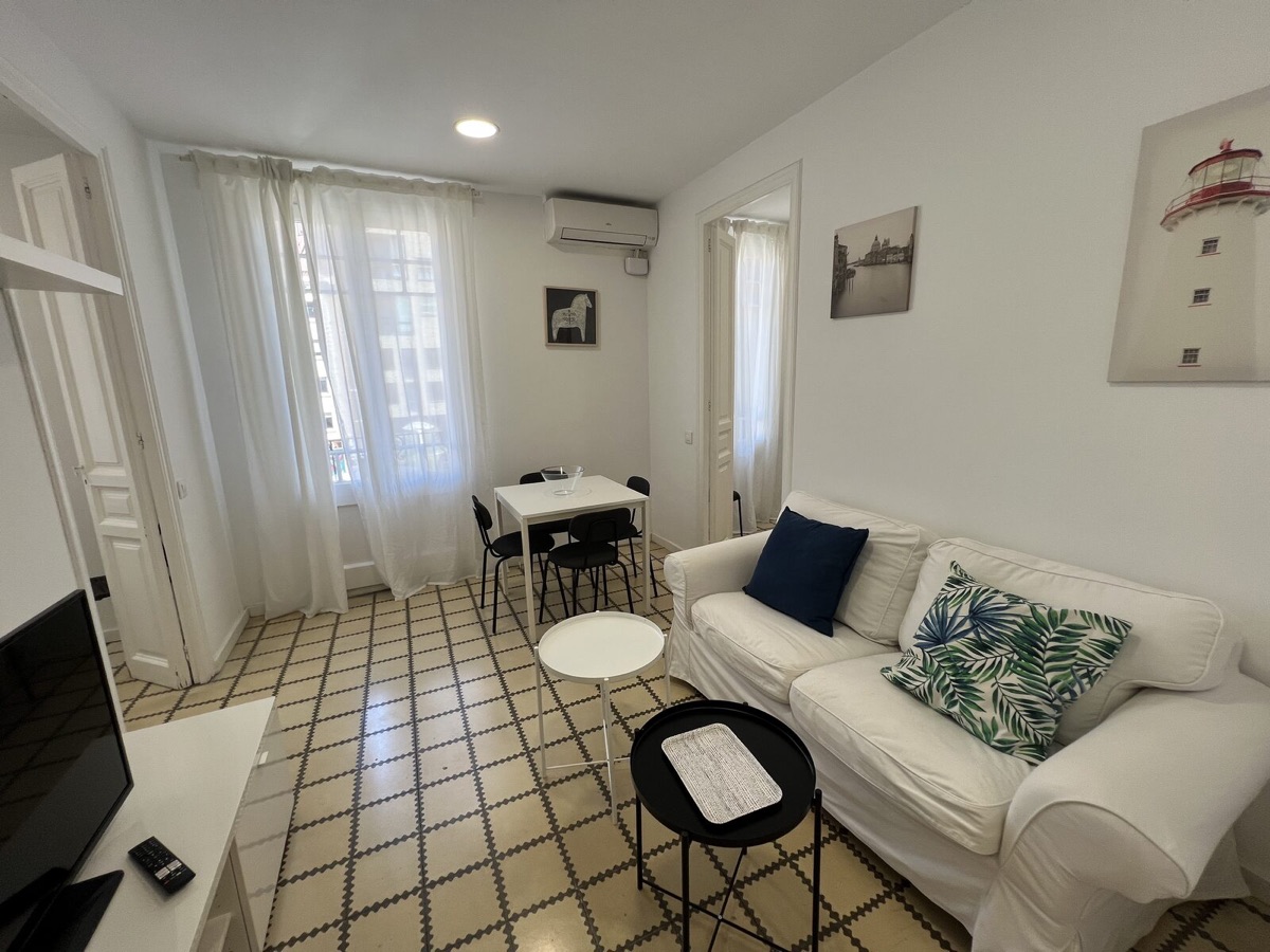 Living room with a patterned tile floor, white sofa and dining table by the balcony